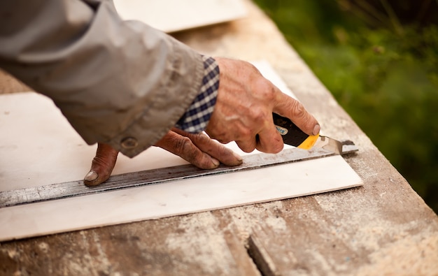 Senior elderly carpenter using a straightedge to draw a line on a board.