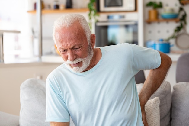 背骨の坐骨神経痛の座りがちなライフスタイルのコンセプトに苦しむ背中に触れるシニアの老人