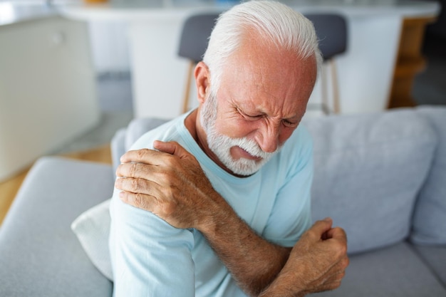 Пожилой мужчина, касающийся своего плеча, страдающий от боли в плече, ишиас, сидячий образ жизни, концепция проблем со здоровьем плеча, медицинская страховка.
