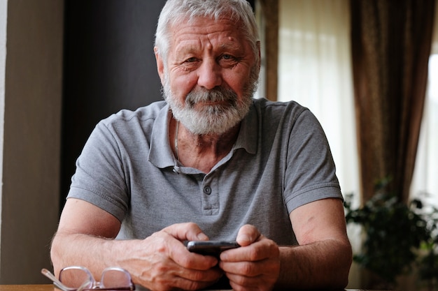 Foto uomo anziano senior con smart phone seduto a casa