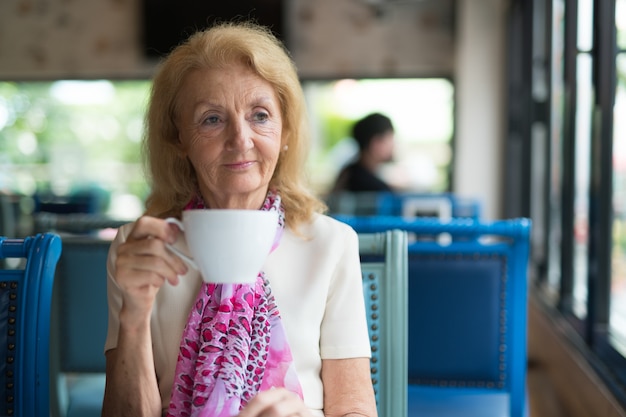 Senior Elderly Woman Drinking Coffee And Looking Out Of Window