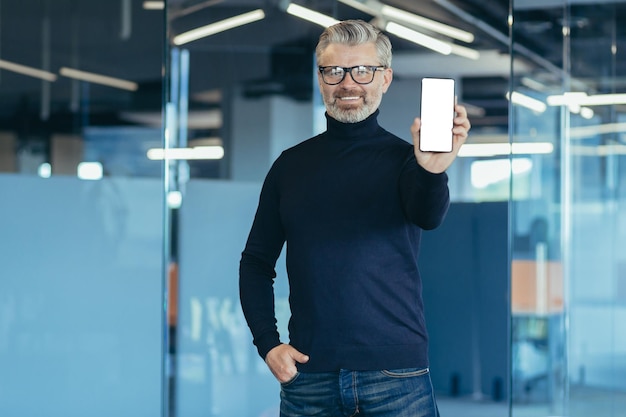 Senior ervaren grijsharige zakenman die in kantoor werkt, portret van een man met een volwassen telefoon