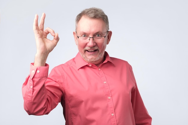 Senior uomo europeo in camicia rossa che mostra segno ok