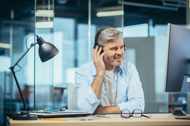 Senior and experienced business man resting at work during a break listening to music from headphones manager working in a modern office