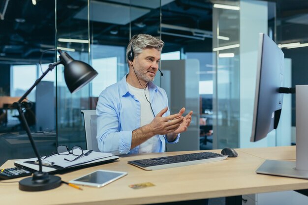 노련하고 노련한 직원이 화상 통화로 구매자에게 조언합니다. 현대 사무실에서 일하는 남자는 협상을 위해 헤드셋과 웹캠을 사용합니다