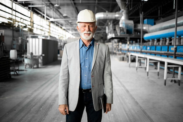 Senior factory CEO or manager in business suit and hardhat walking through industrial production department and checking manufacture process.