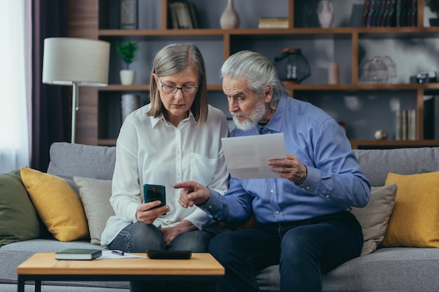 Senior familie paar grijze haren oude man en vrouw betalen voor diensten gegevensdocumenten invoeren met behulp van applicatie mobiele smartphone Gepensioneerden thuis nutsrekeningen cheques gebruiken computer slimme telefoon