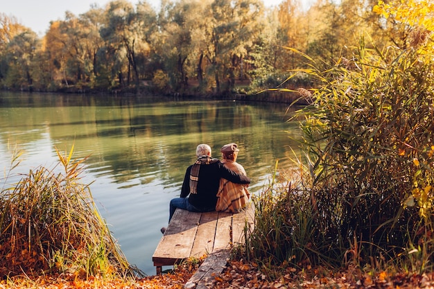 Foto una coppia di anziani che si rilassano al lago d'autunno un uomo e una donna che si godono il paesaggio seduti sul molo