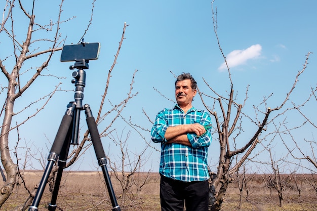 Старший фермер ведет видеоблог в саду, современный фермер использует социальные сети