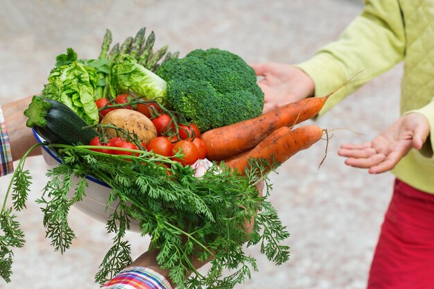 Senior farmer man holding in hands harvest from his orchard and giving it to young boy Assortment of ripe homegrown vegetables Organic market bio food delivery zero waste ecofriendly concept