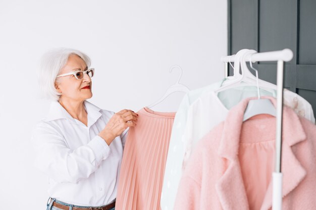 Eleganza senior della moda. collezione showroom. signora anziana intelligente al rack di vestiti alla moda.