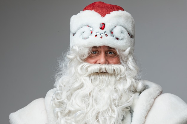 Senior father frost met versierde wintermuts en witte lange baard die naar de camera kijkt en lacht met zijn vriendelijke ogen.