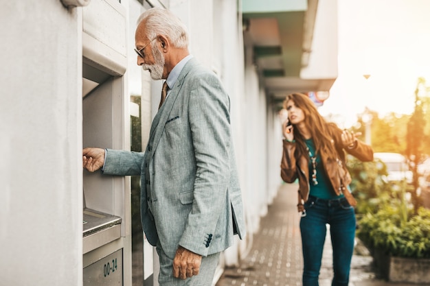 Padre anziano e sua figlia che usano insieme il bancomat per prelevare denaro. loro sono felici. luminosa giornata di sole.