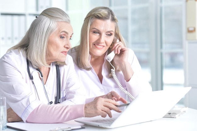 Senior female doctor and her colleague using laptop and talking on the phone