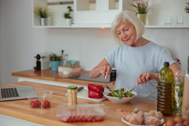 Senior female making salad at home kitchen