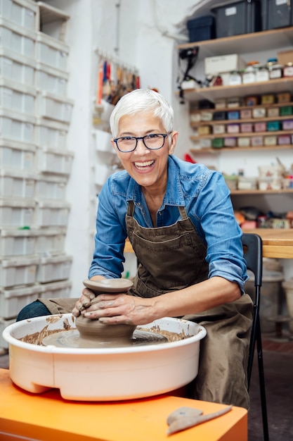 Photo senior female potter working on pottery wheel while sitting  in her workshop