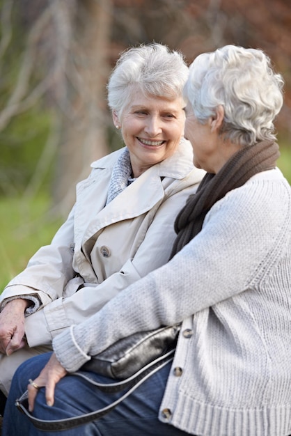 Amici anziani amano e parlano all'aperto in natura insieme e strettamente legati alla pensione in vacanza le donne anziane sorridono o si guardano in faccia in campagna felici o sociali con cura sulla roccia