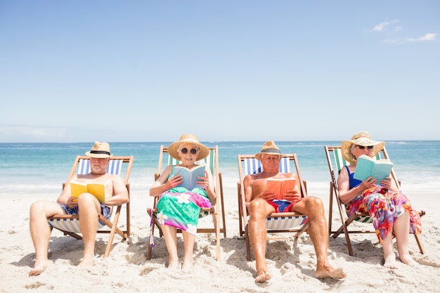 Libri di lettura senior degli amici sulla sedia di spiaggia