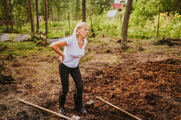 Senior gardener woman falls hurts back pain radiculitis digging at summer farm countryside outdoors