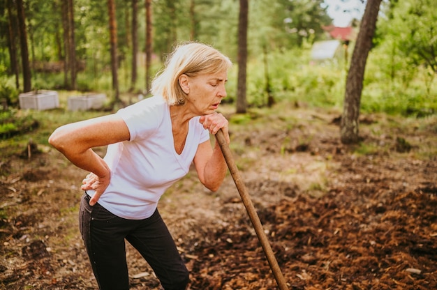 Senior gardener woman falls hurts back pain radiculitis digging at summer farm countryside outdoors