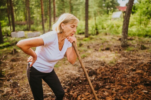 Senior gardener woman falls hurts back pain radiculitis digging at summer farm countryside outdoors