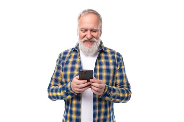 Senior gepensioneerde grijsharige man met een baard in een shirt beheerst een smartphone op een witte achtergrond