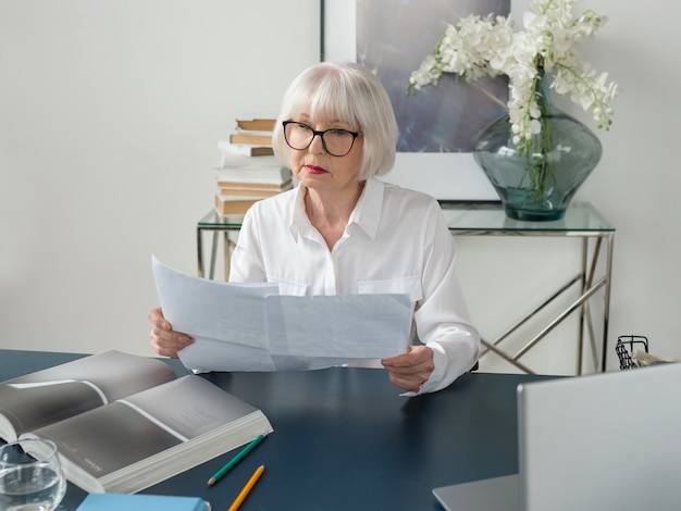 senior gray hair woman in white blouse reading documents in office