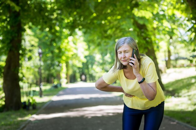 Senior grayhaired woman in the park on a walk feeling unwell calls the doctor by phone