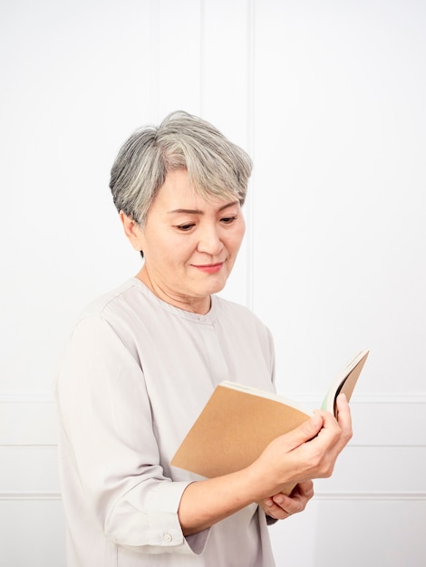 Senior grey hair Asian woman holding and reading book at home.