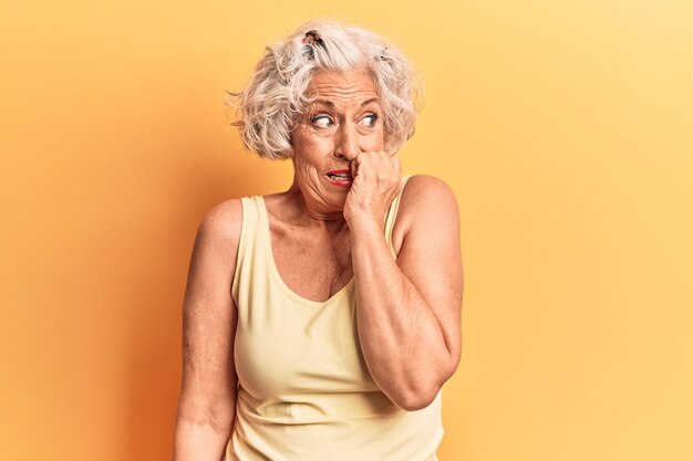 Senior grey-haired woman wearing casual clothes looking stressed and nervous with hands on mouth biting nails. anxiety problem.