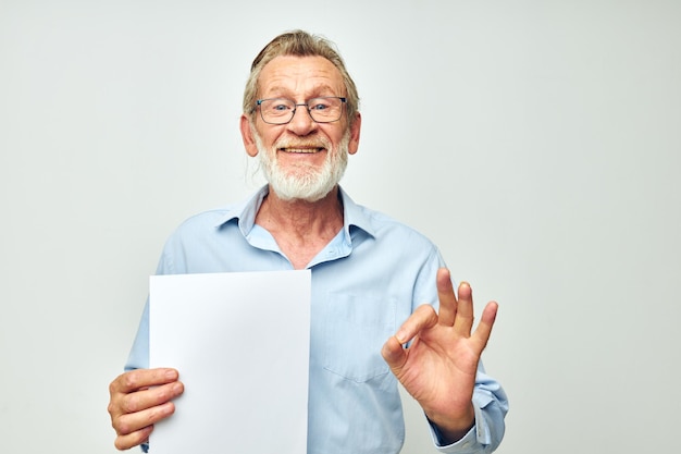 Senior greyhaired man blank sheet of paper gesture hands smile\
light background