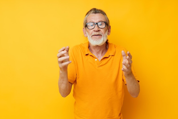 Senior greyhaired man posing yellow tshirt glasses yellow background