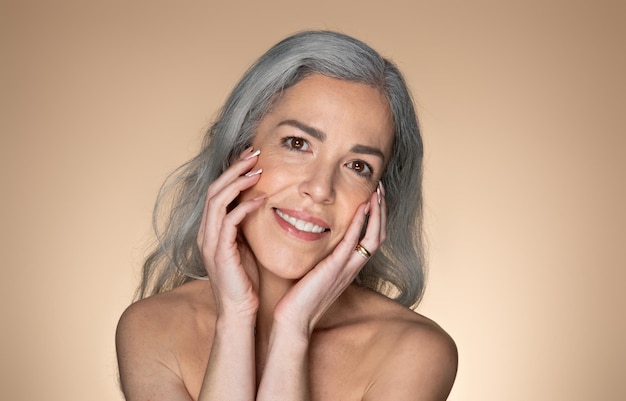 Senior greyhaired woman touching her face and smiling at camera doing morning face care routine