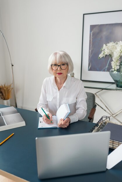 senior grijs haar vrouw in witte blouse lezen van documenten in office