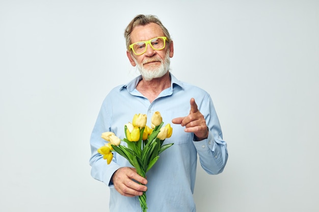 Senior grijsharige man in een blauw shirt met een boeket bloemen lichte achtergrond