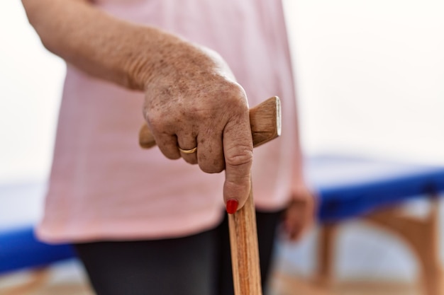 Senior grijsharige vrouwelijke patiënt die steunt met wandelstok in de kliniek voor fysiotherapie