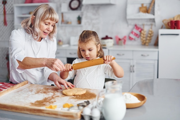 Senior grootmoeder met haar kleine kleindochter kookt snoep voor Kerstmis in de keuken