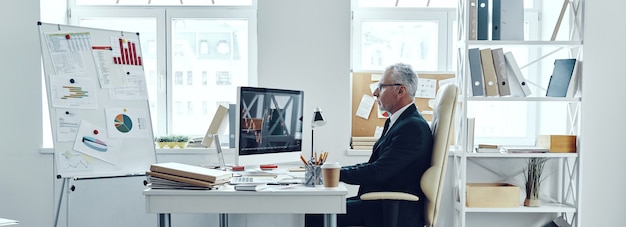 Senior handelaar in elegant pak met computer tijdens het werken op kantoor