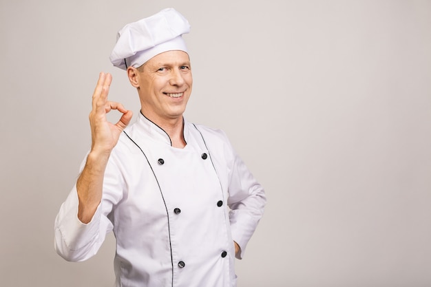 Senior handsome chef cook isolated on grey wall. Ok sign.