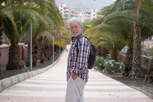 Senior handsome man walking in the city public park relaxing looking at camera smiling