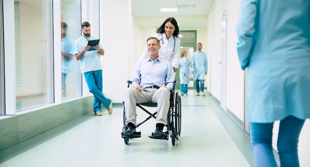 Senior handsome man in a wheelchair is moving in the hospital with help of medical special staff