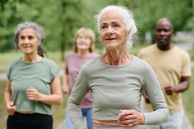 Photo senior healthy woman running outdoors with other people in background