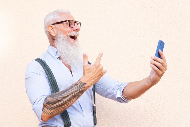 Senior hipster man met tatoeage plezier met een telefoon geluk technologie en ouderen levensstijl mensen concept