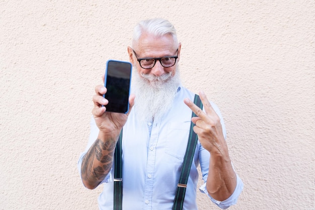 Senior hipster man with tatoo having fun with a phone, showing it, happiness, technology and elderly lifestyle people concept