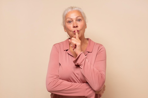 Senior hispanic woman saying hush be quiet with finger on lips