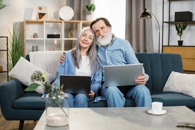 Senior husband and wife holding a laptops in their laps and surfing the Internet together