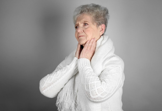 Senior donna malata con mal di gola su sfondo grigio. concetto di allergia