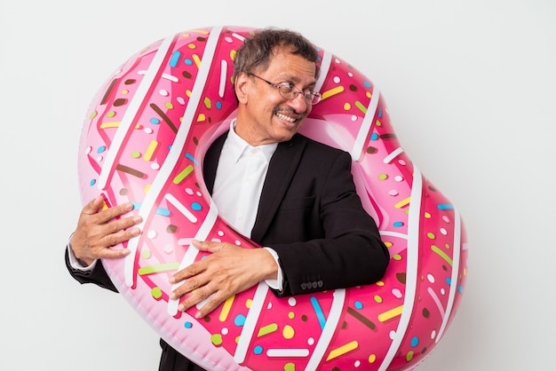 Senior indian business man holding inflatable donut isolated on white background looks aside smiling, cheerful and pleasant.