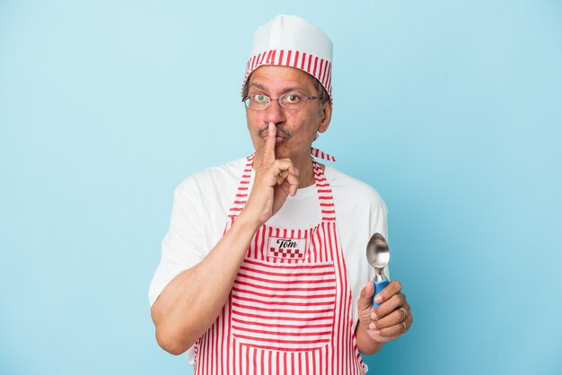 Senior indian ice cream man holding a scoop isolated on blue background keeping a secret or asking for silence.