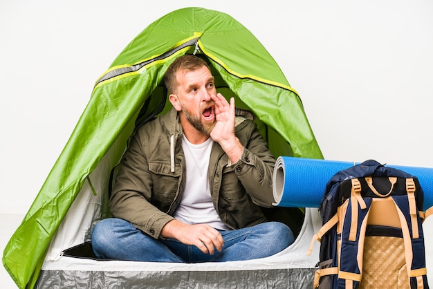 Senior inside a tent isolated on white shouting and holding palm near opened mouth.